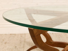 Load image into Gallery viewer, Close-up of a round glass-top table with a green-tinted glass rim and a curved wooden base, shown against a light neutral background.
