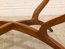Load image into Gallery viewer, Close-up of a mid-century modern wooden table base with curved legs and a polished finish, resting on a textured beige rug.
