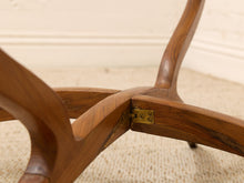 Load image into Gallery viewer, Close-up of a wooden chair base with curved legs and a brass-colored metal hinge, set on a beige carpeted floor against a cream wall.
