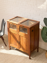 Load image into Gallery viewer, Antique wood display cabinet with glass-top surface, glass-front upper doors, paneled lower cabinet doors, and aged brass hardware.
