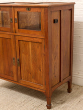 Load image into Gallery viewer, A vintage wooden display cabinet with glass-front upper doors, solid wood lower doors, brass-style hardware, and turned legs, shown against a white brick wall and textured rug.
