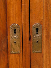 Load image into Gallery viewer, Close-up of two warm brown wooden doors with ornate brass keyhole hardware and matching metal plates.

