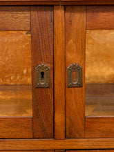 Load image into Gallery viewer, Close-up of a wooden cabinet with two central doors, brass keyhole hardware, and warm brown wood grain with glass panels on either side.

