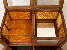 Load image into Gallery viewer, An antique wooden display case with a hinged lid, featuring gold velvet lining and glass panels, photographed open against a white brick wall.
