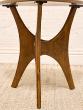 Load image into Gallery viewer, A mid-century modern wooden table base with a warm brown finish, featuring a central vertical post and three splayed legs, shown on a textured rug against a white brick wall.
