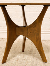 Load image into Gallery viewer, A close-up of a mid-century modern wooden table base with curved legs and a light wood tabletop, set against a white brick wall and textured rug.
