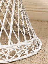 Load image into Gallery viewer, A close-up of a white woven rattan or wicker chair base with a geometric lattice design, resting on a textured beige woven rug.
