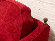 Load image into Gallery viewer, A close-up of a red textured fabric armchair or sofa corner with a dark wooden finial on the arm, set against a white painted brick wall.
