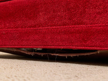 Load image into Gallery viewer, Close-up of a red textured fabric cushion or upholstered furniture edge resting on a beige carpeted floor, with visible frayed wear at the bottom.
