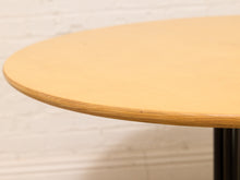 Load image into Gallery viewer, Close-up of a round light wood table top with a visible edge profile, set against a white painted brick wall background.
