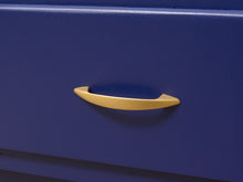 Load image into Gallery viewer, A close-up of a modern, curved pull handle in a matte mustard yellow finish mounted on a dark blue drawer or cabinet door.
