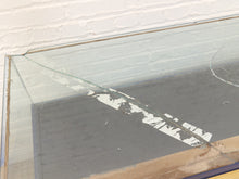 Load image into Gallery viewer, A large rectangular glass tabletop or display case with a severely cracked and broken glass surface, photographed against a white painted brick wall.
