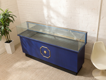 Load image into Gallery viewer, Vintage black and gold retail display counter with long glass showcase top and decorative gold medallion
