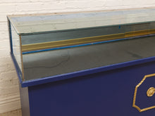 Load image into Gallery viewer, A vintage blue display case with a glass top and gold trim, photographed against a white brick wall.
