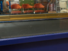 Load image into Gallery viewer, A close-up of a dark gray or black textured surface, likely a countertop or protective film, bordered by a blue frame and a gold trim, with a blurred background showing orange chairs.
