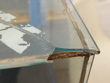 Load image into Gallery viewer, Close-up of a broken glass tabletop corner with chipped, cracked glass and a worn brown filler strip along the edge.

