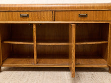 Load image into Gallery viewer, A mid-century modern wooden sideboard or credenza with two drawers on top, three open shelves inside, and one front door panel open, shown on a textured beige carpet against a white brick wall.
