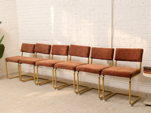 Load image into Gallery viewer, Six matching mid-century modern dining chairs with rust-brown corduroy upholstery and gold-finished metal frames, arranged in a row against a white brick wall.
