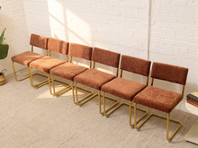 Load image into Gallery viewer, Six matching dining chairs with brown corduroy upholstered seats and backs and gold metal frames, arranged in a row against a white brick wall.
