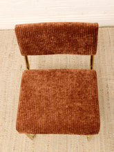 Load image into Gallery viewer, A modern accent chair with a rust-brown ribbed corduroy fabric seat and backrest, supported by slim gold metal legs, photographed from a top-down angle on a woven rug.
