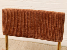Load image into Gallery viewer, A close-up of a mid-century modern chair featuring a rust-brown ribbed corduroy upholstered backrest and gold-finished metal legs, set against a white brick wall background.
