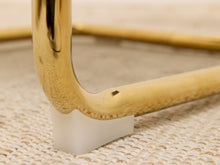 Load image into Gallery viewer, Close-up of a gold metal furniture leg with a white plastic wedge base on a woven beige surface.
