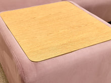 Load image into Gallery viewer, A square light wood-grain mat with rounded corners, laid flat on top of a dusty pink upholstered ottoman or stool.
