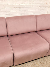 Load image into Gallery viewer, A close-up of a blush pink velvet modular sofa seat and back cushions against a white brick wall background.

