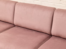 Load image into Gallery viewer, A close-up of a dusty pink velvet sofa with clean channel tufting and a white brick wall background.
