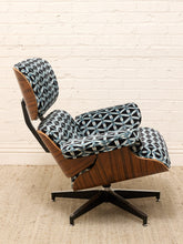 Load image into Gallery viewer, A mid-century modern lounge chair with patterned blue and white fabric upholstery and a wood-grain shell, set against a white brick wall and beige rug.
