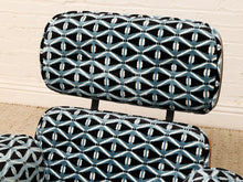 Load image into Gallery viewer, Close-up of upholstered chair cushions with a black background and a repeating geometric diamond pattern in light blue and white, set against a cream brick wall and beige carpet.
