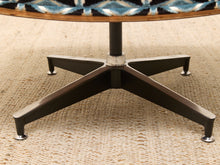 Load image into Gallery viewer, Close-up of a mid-century modern round table base with a five-star metal pedestal frame and a patterned blue, black, and beige seat cushion, set on a woven beige rug.
