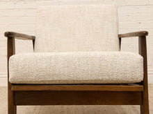 Load image into Gallery viewer, A mid-century modern armchair with a textured cream bouclé seat cushion and backrest, supported by a warm brown wooden frame, set against a white brick wall.
