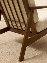 Load image into Gallery viewer, Close-up of a mid-century modern wooden armchair with a slatted backrest and textured beige fabric cushions, set on a woven beige rug.
