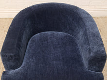 Load image into Gallery viewer, A close-up of a navy blue velvet armchair, showing the rich textured fabric and curved backrest, set against a neutral indoor background with a beige rug and white wall.
