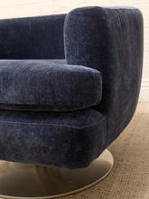 Load image into Gallery viewer, Close-up of a modern upholstered armchair in dark navy blue velvet fabric, showing the seat cushion, backrest, and a round metallic base on a woven rug.
