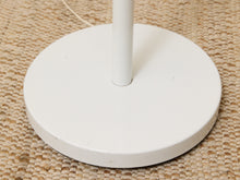 Load image into Gallery viewer, A close-up of a white round lamp base with a central pole, resting on a woven beige rug.
