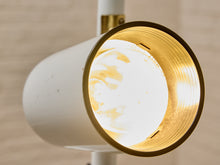 Load image into Gallery viewer, Close-up of a modern cylindrical wall lamp with a white outer shade and a gold-toned interior, shown lit against a softly blurred beige background.
