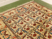 Load image into Gallery viewer, A traditional patterned area rug with a beige background, featuring red, blue, and brown floral motifs and a cream fringe, laid out on a green floor.
