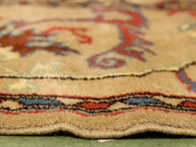 Load image into Gallery viewer, Close-up of a patterned area rug with a beige base and red, blue, and brown motifs, showing the textured pile and scalloped edge.
