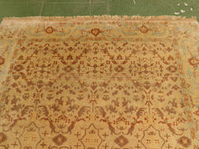 Load image into Gallery viewer, A square area rug with a traditional floral and geometric pattern in beige, rust red, and light blue, laid out on a green floor.
