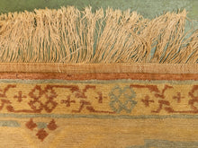Load image into Gallery viewer, Close-up of a woven rug showing beige fringe, a rust-brown patterned band, and a muted blue-green background field.
