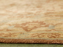 Load image into Gallery viewer, Close-up of an area rug showing its textured brown pile and a faded beige and light blue traditional floral pattern.
