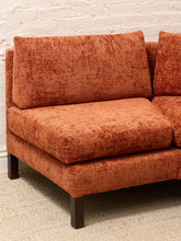 Load image into Gallery viewer, A close-up of a modern upholstered sofa section in a textured rust-orange fabric, shown against a white brick wall and light beige carpet.
