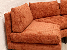 Load image into Gallery viewer, An orange textured bouclé sectional sofa corner with matching back cushions, shown against a white brick wall.
