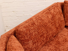 Load image into Gallery viewer, Close-up of a textured terracotta orange upholstered sofa with a white painted brick wall background.
