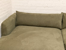 Load image into Gallery viewer, An olive green textured slipcover fitted over a sofa, shown in a corner against a white brick wall.
