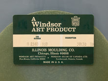 Load image into Gallery viewer, A vintage dark green and beige identification card for Windsor Art Products, manufactured by Illinois Moulding Co., placed on top of a textured olive-green circular object against a neutral gray background.

