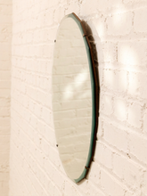 Load image into Gallery viewer, An oval wall mirror with a dark green glass edge and a dark brown wooden frame, mounted on a white painted brick wall.
