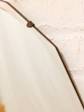Load image into Gallery viewer, Close-up of a large off-white mirror with a dark brown metal frame and a small metal bracket, set against a textured off-white plaster wall.
